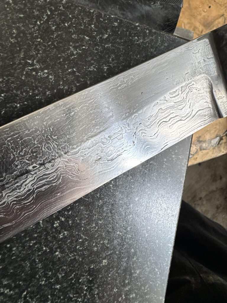 Close view of the layered patterned steel finish on the Sabatier-style knife blade